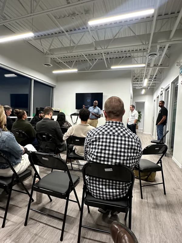 A wide view of the room from the back, with several attendees gathered standing near the entrance.