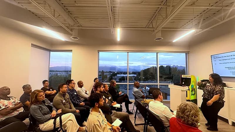 Wide view of the FV+AI meetup room during a talk, with sunset over the mountains through a wall of windows.