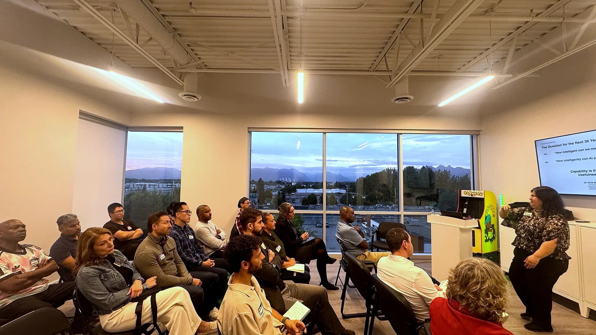 Wide view of the FV+AI meetup room during a talk, with sunset over the mountains through a wall of windows.