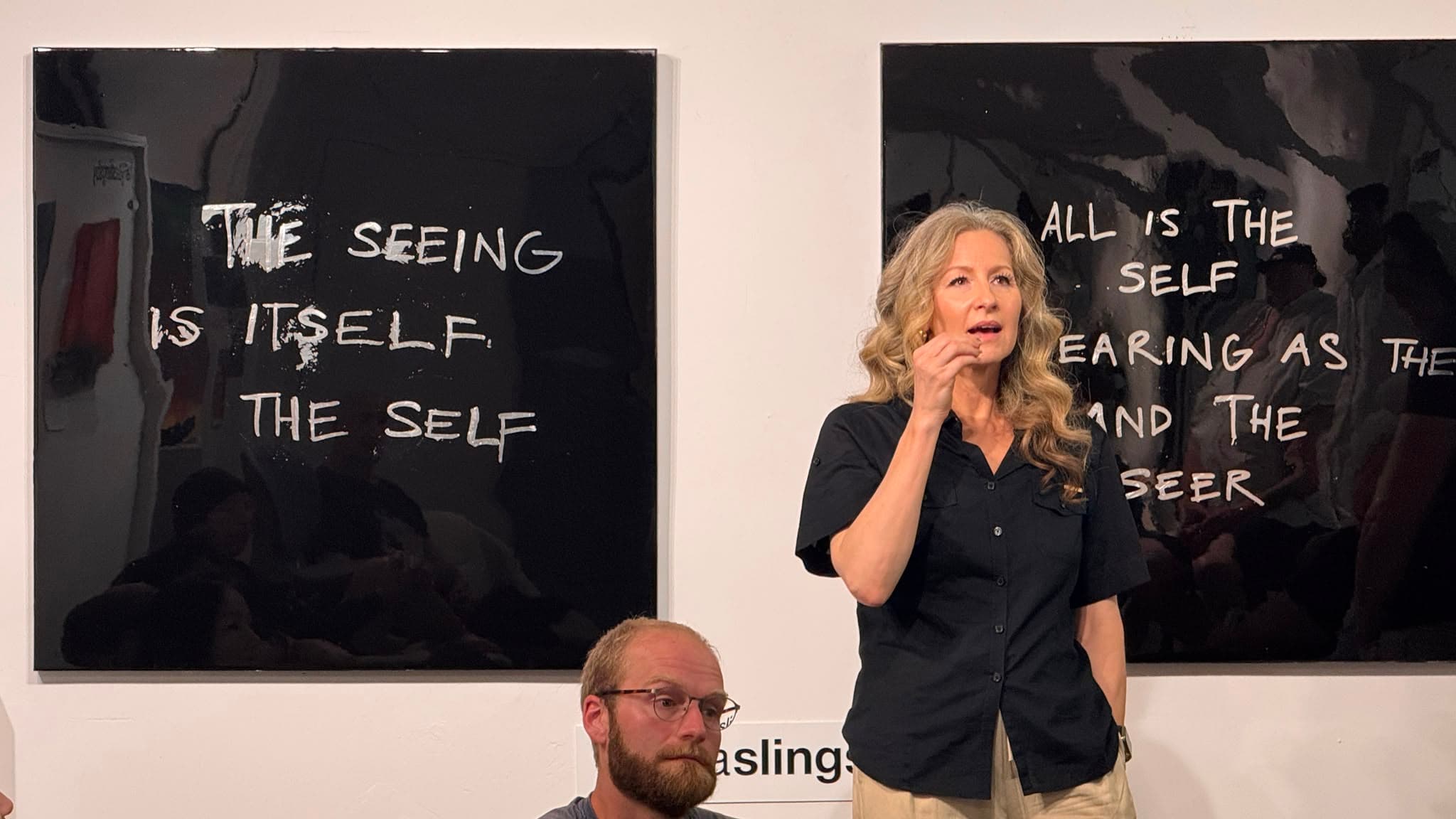 A speaker addresses AI Ethical Futures Lab beside gallery works about perception and the self.