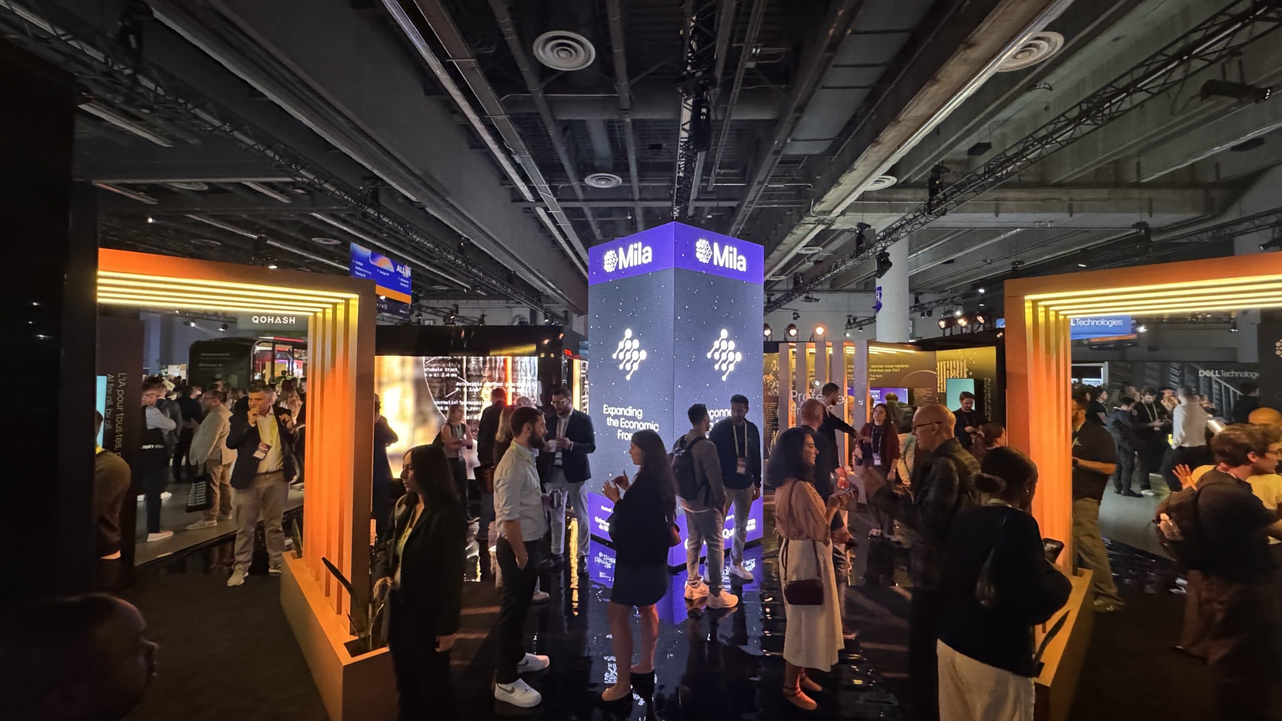 Attendees talking around the illuminated Mila pavilion on the ALL IN expo floor.