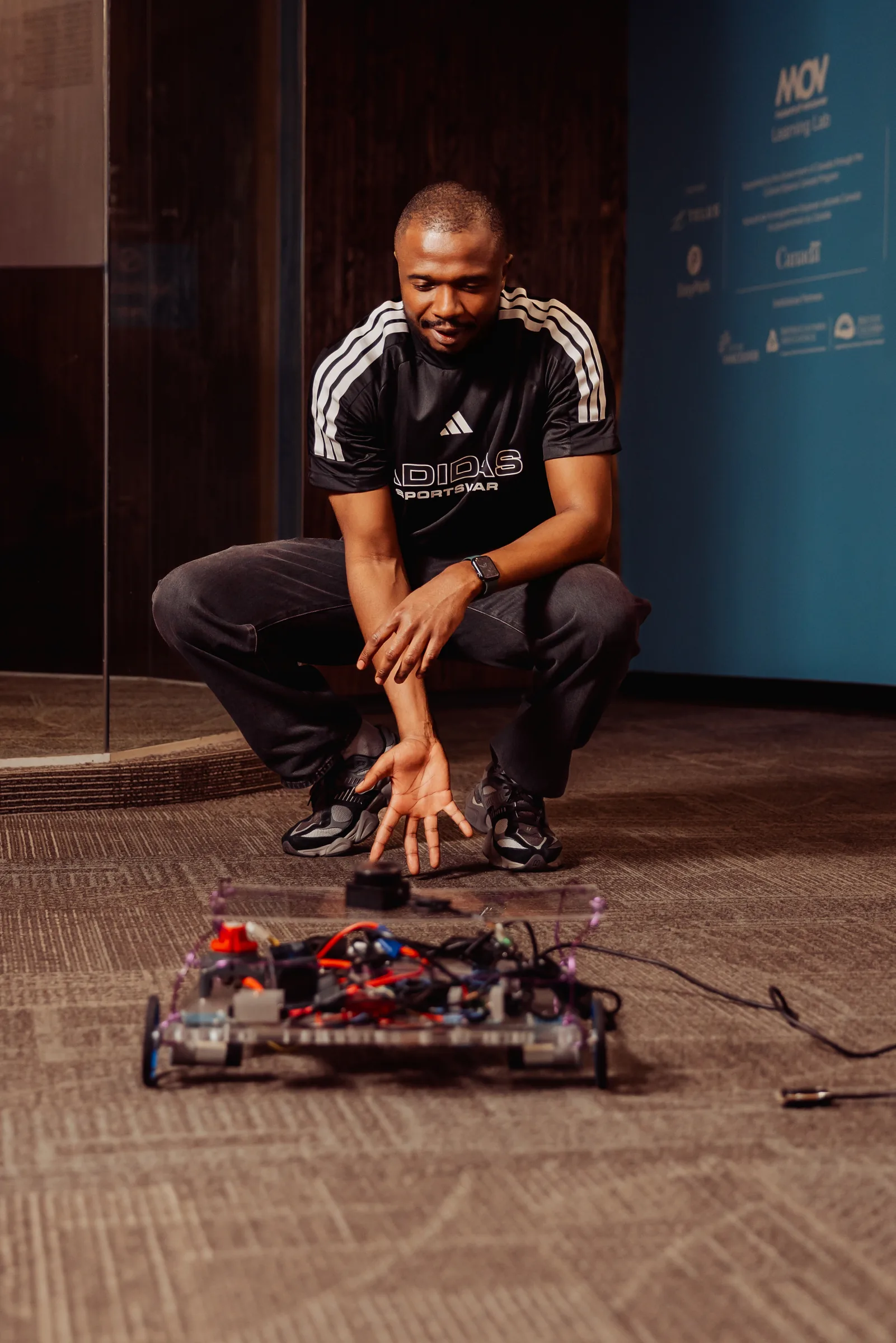 A presenter crouches beside a wheeled robot during a live Vancouver AI demo.