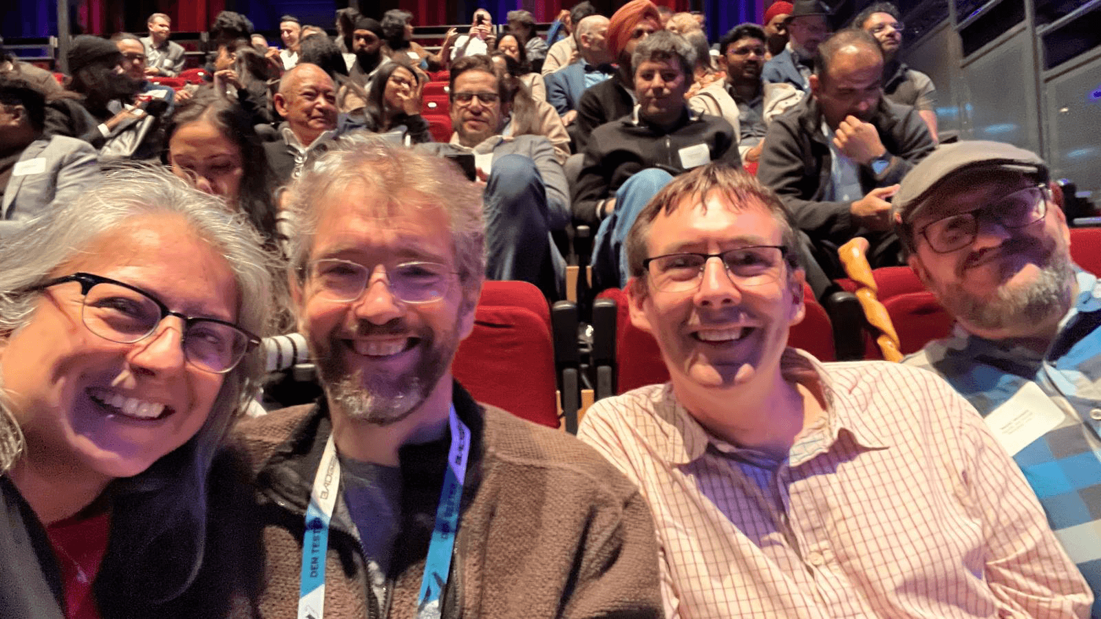 Group selfie at AI vs. Human, with red theatre seating and the audience behind.