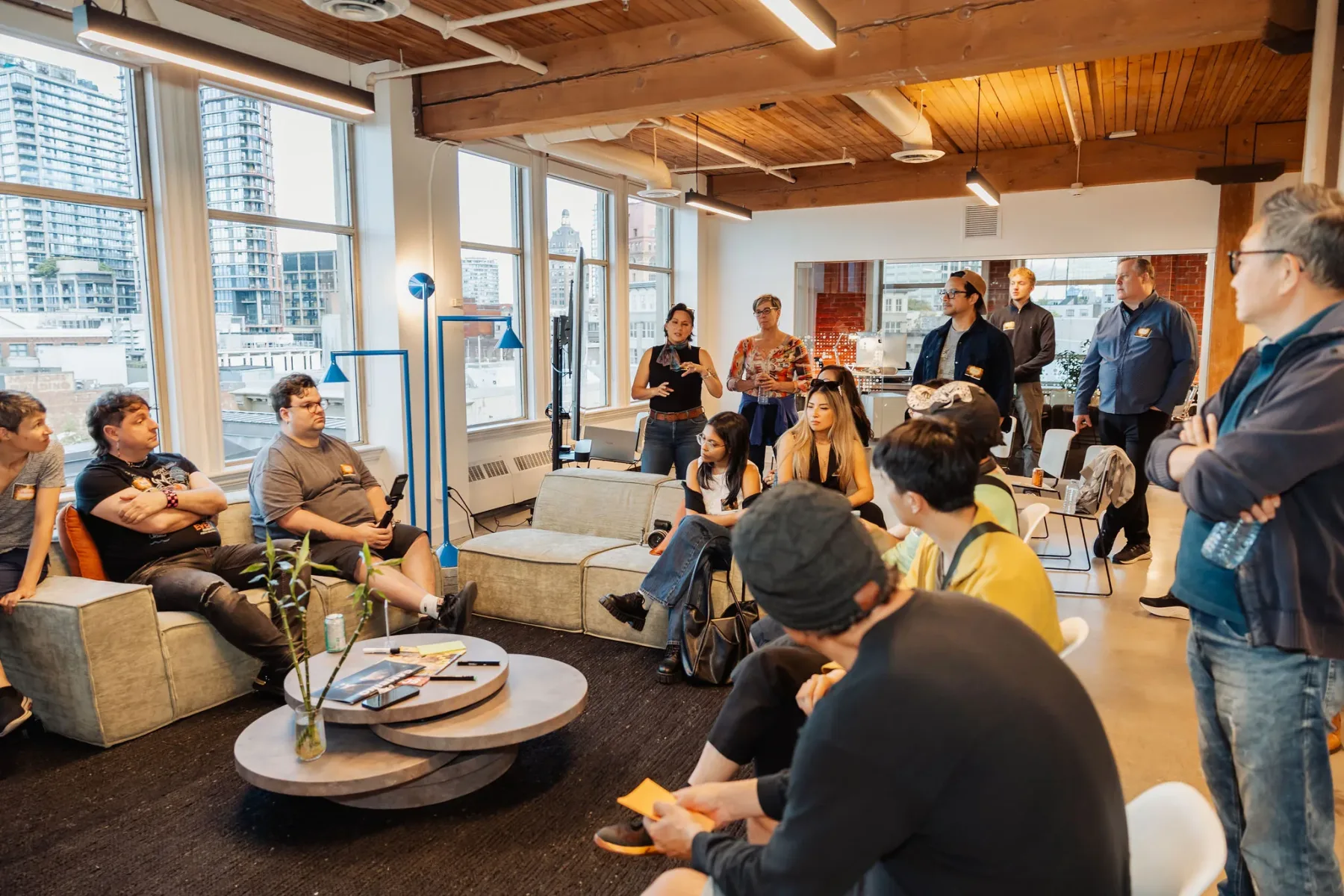 People gathered in a circle on low couches in a Vancouver studio loft, mid-conversation. Archive photograph from the wider BC + AI ecosystem; this forming group has not run its own session yet.