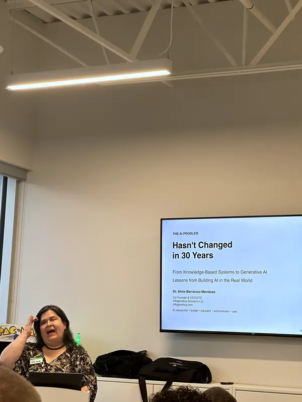 Dr. Alma Barranco-Mendoza gestures while presenting beside a slide titled "Hasn't Changed in 30 Years," tracing the line from knowledge-based systems to generative AI.