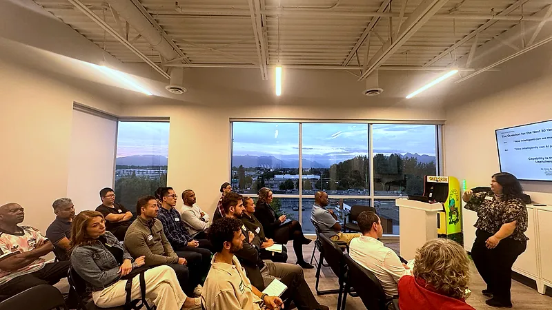 Wide view of the FV+AI meetup room during a talk, with sunset over the mountains through a wall of windows.