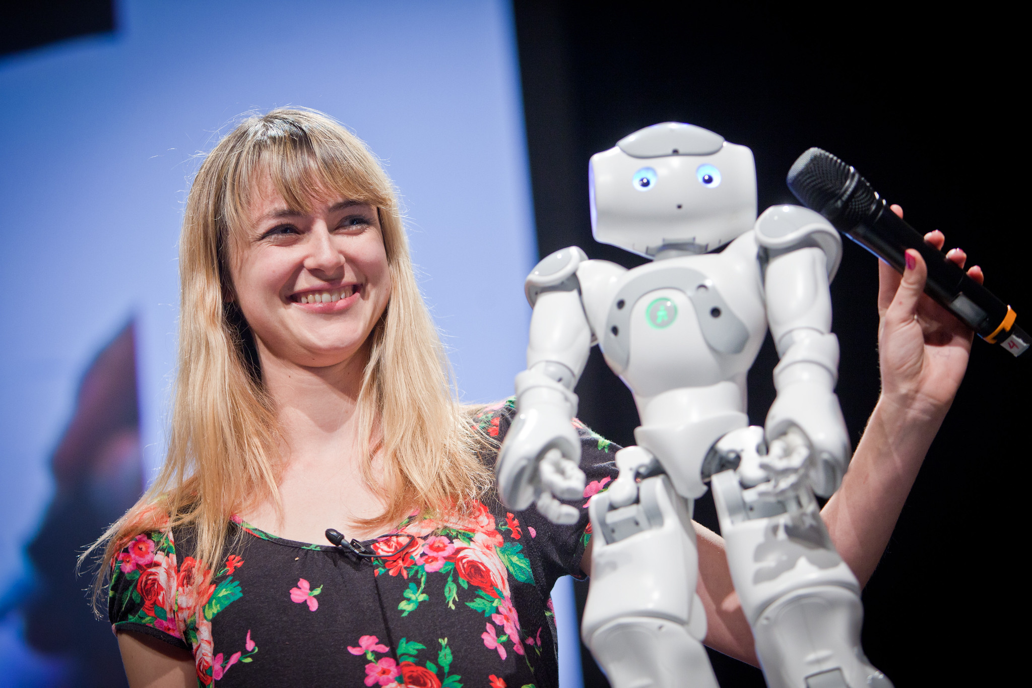 Heather Knight holds a microphone toward Data, a small humanoid robot, onstage at PopTech.