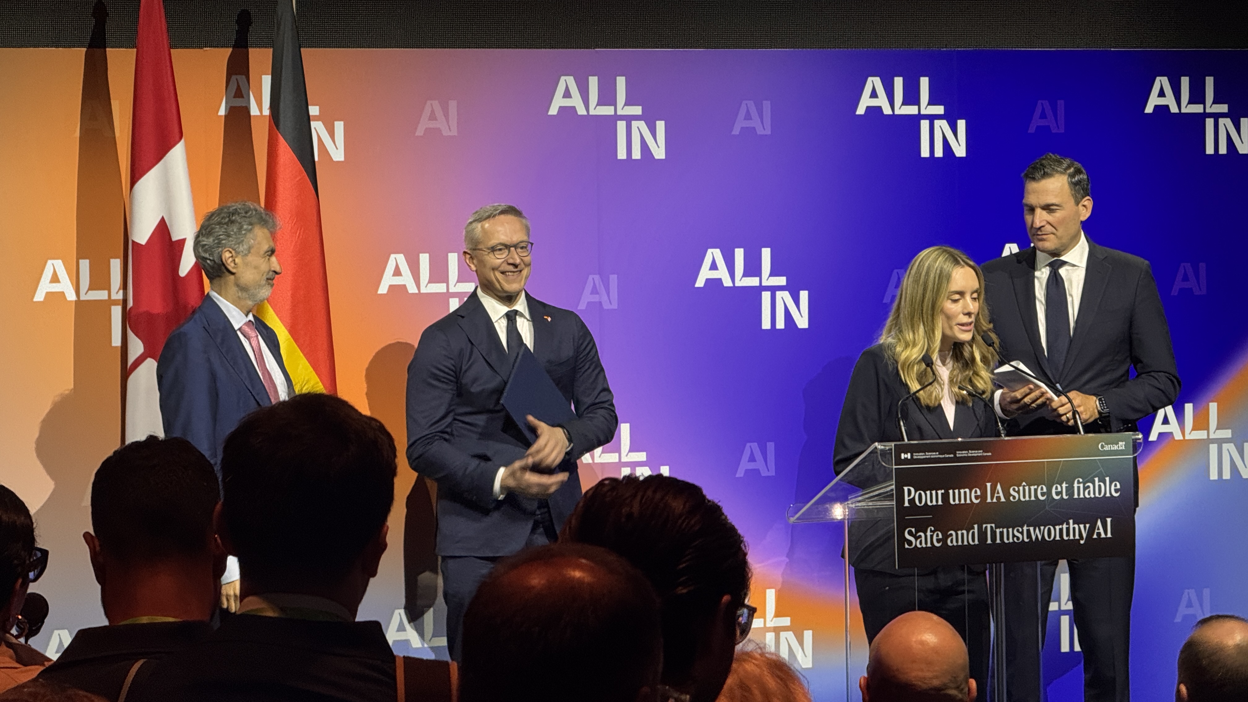 Justine Gauthier at the Safe and Trustworthy AI podium, with Yoshua Bengio, Karsten Wildberger and Evan Solomon on stage.